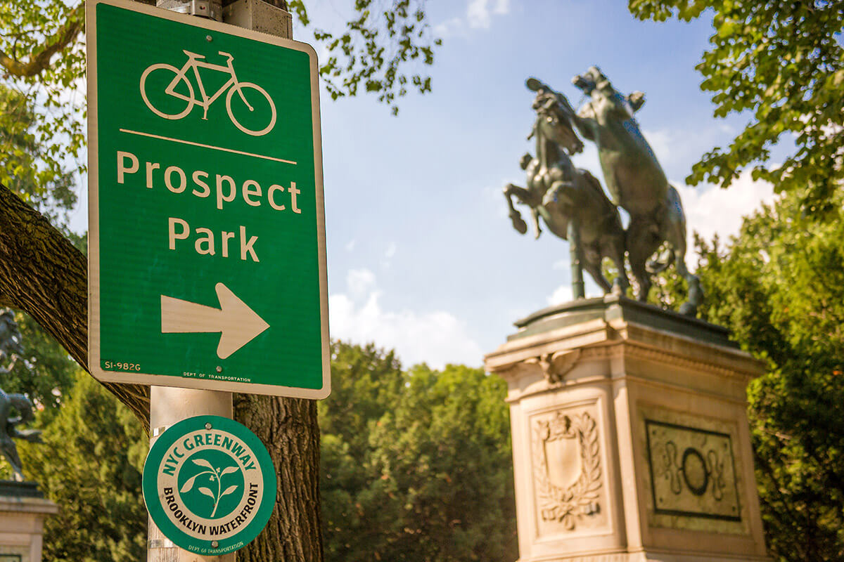 Sign with directions to Prospect Park's bike path with The Horse Tamers monument in the background