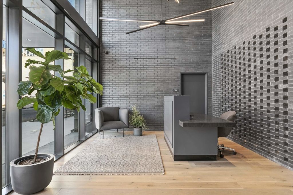 555 Waverly's Lobby with walls of grey brick and a fiddle leaf plant in the front corner.
